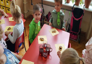 słodki poczęstunek przy stoliku dla dzieci: ciasteczka z dżemem leżą na białych serwetkach a na środku stoją soki w szklankach